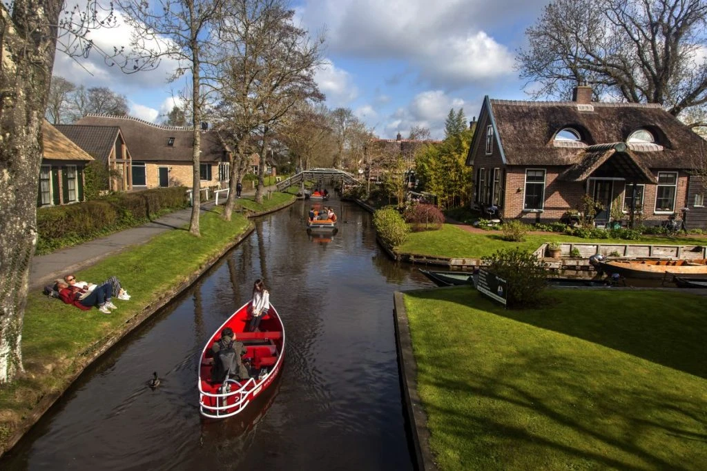 casal deitado na grama tomando sol na beira do canal enquanto vê um barco passeando pelo canal de Giethoorn, a Veneza da Holanda
